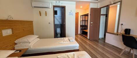 A hotel room with two beds, a wooden headboard, a desk, and a bathroom visible through an open door.