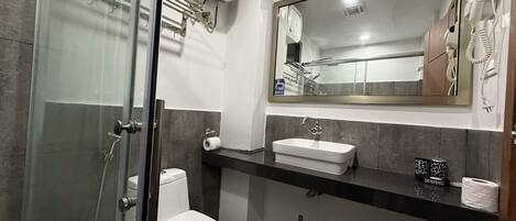 Ein Badezimmer mit Duschkabine aus Glas, einer weißen Toilette, einem Waschbecken mit Spiegel und einem Handtuchhalter.