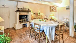 A dining area with a round table, chairs, a fireplace, and a painting on the wall.