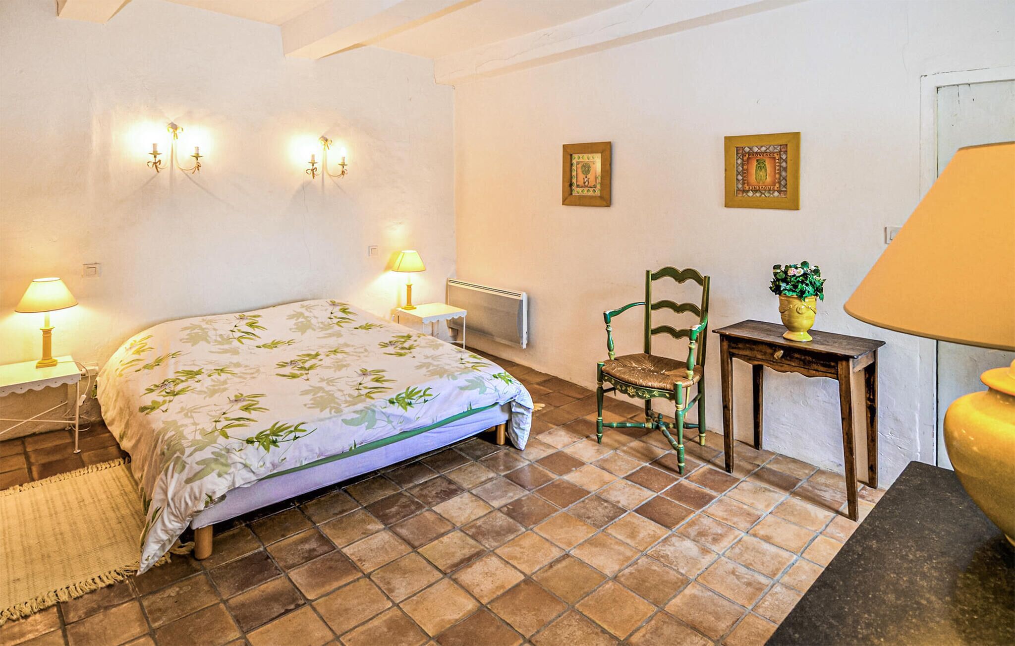 A bedroom with a bed, two wall-mounted lamps, a chair, a small table with a plant, and a radiator.