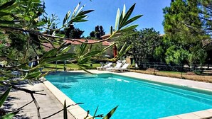 A clear blue swimming pool with lounge chairs and a tiled deck.