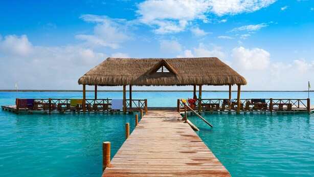 A wooden pier leading to a thatched-roof overwater bungalow with a pool and lounge chairs. - Maya Heaven Penthouse in Tulum with Private Rooftop, Pool & Parking (Tulum)