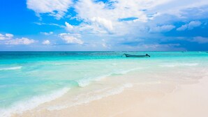 A beach with clear turquoise water and a boat in the distance. - Maya Heaven Penthouse in Tulum with Private Rooftop, Pool & Parking (Tulum)