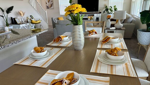 Un comedor con una mesa larga dispuesta para cuatro personas, con individuales a rayas y platos blancos.