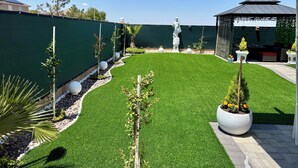 Un patio trasero bien cuidado con césped artificial, una pérgola y una estatua.