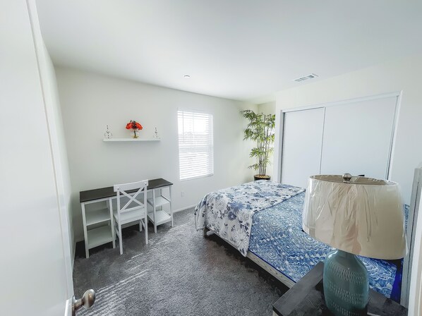 A bedroom with a bed, a desk, a chair, a potted plant, and a window with blinds. - Charming 3-bedroom house with WiFi and AC in delightful Victorville (Victorville)