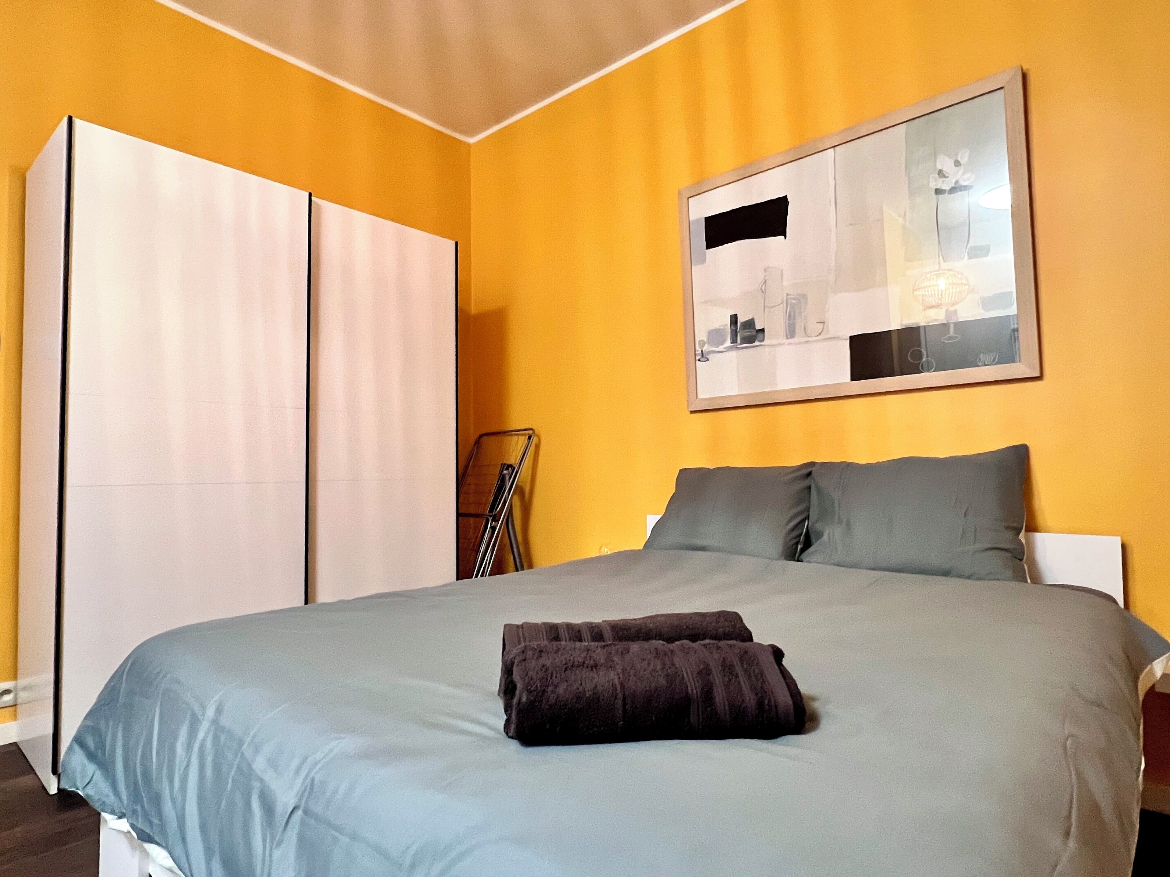 Een slaapkamer met een bed, kussens, een deken, een spiegel en een kledingkast.