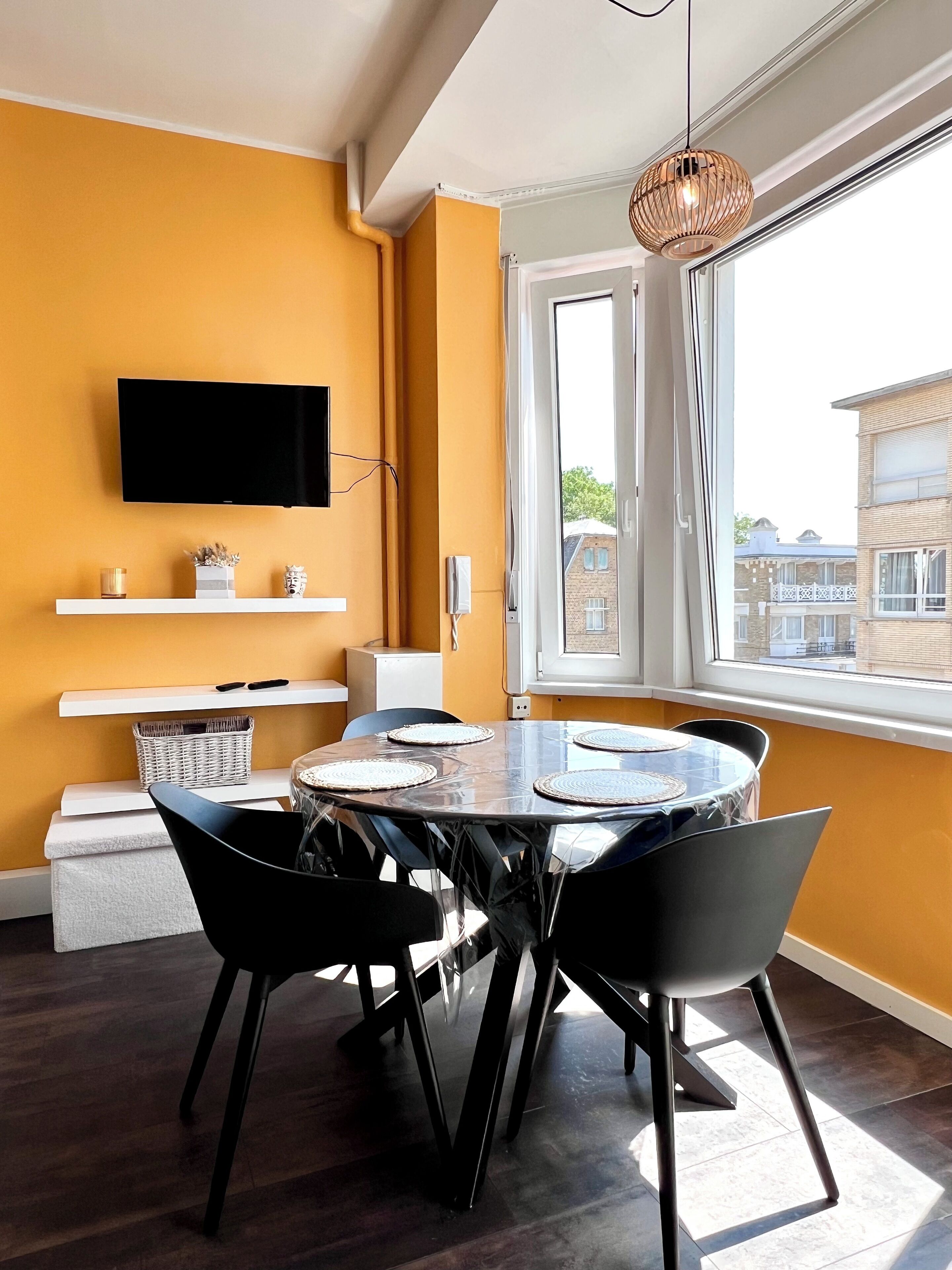 A modern dining area with a round table, black chairs, and a mounted TV.