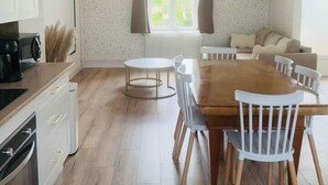 Una cocina moderna con armarios de madera, una mesa de comedor con sillas, una mesa redonda para desayunos y una ventana con cortinas.
