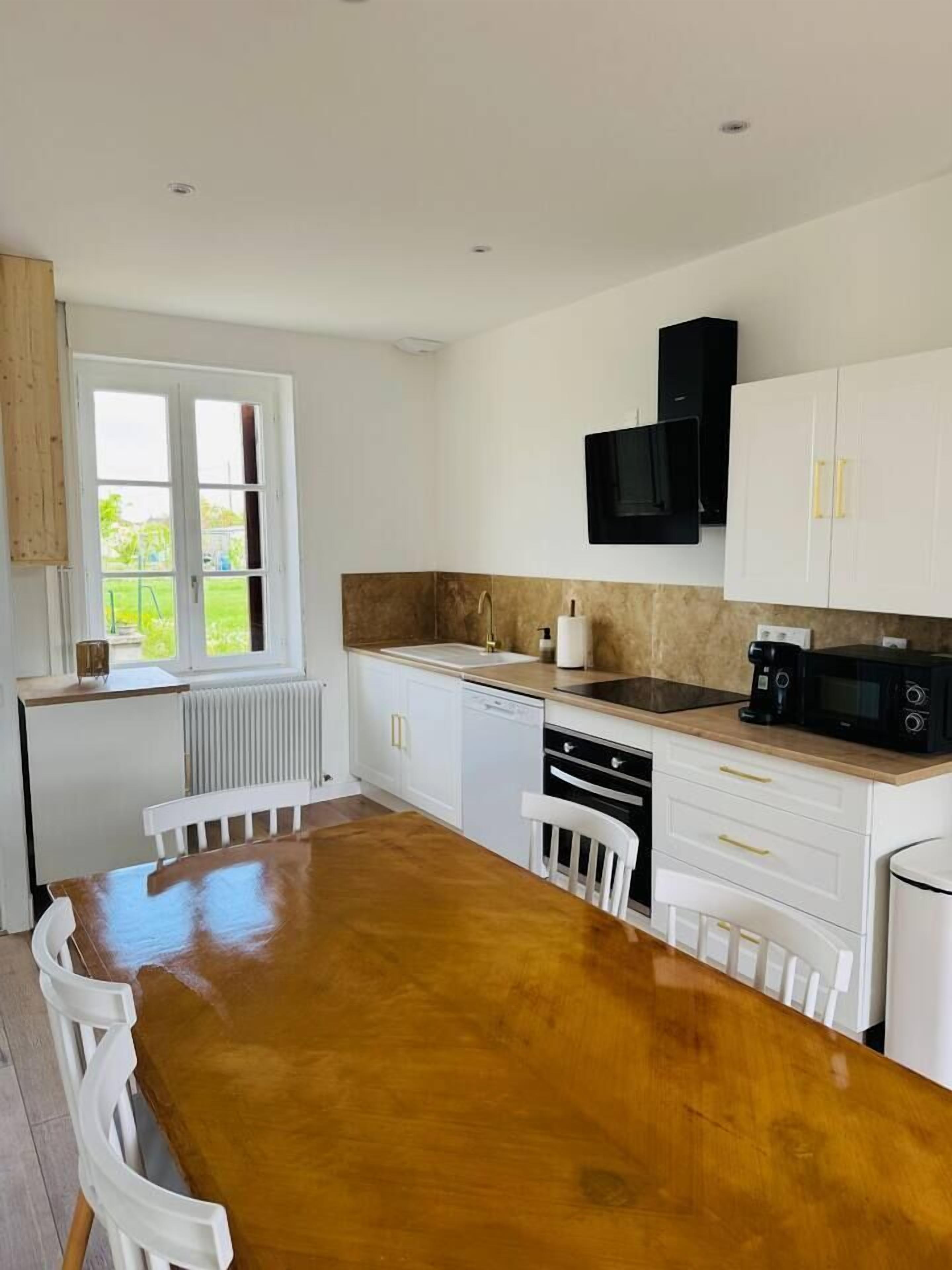 A modern kitchen with white cabinets, a wooden dining table, and a built-in microwave.