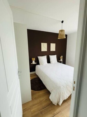 A bedroom with a large bed, a dark accent wall, two bedside tables with lamps, and a hanging light fixture.