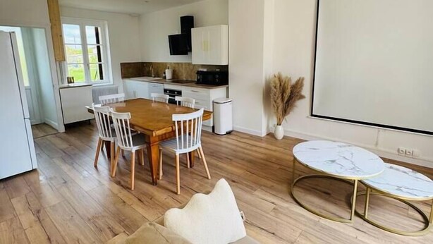 Una sala de estar moderna con una mesa de comedor de madera, sillas blancas, un sofá beige y una pequeña mesa redonda con encimera de mármol.