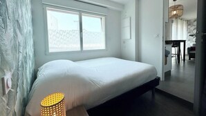Ein modernes Schlafzimmer mit einem großen Bett, einer Nachttischlampe und Blick auf einen Essbereich durch eine offene Tür.