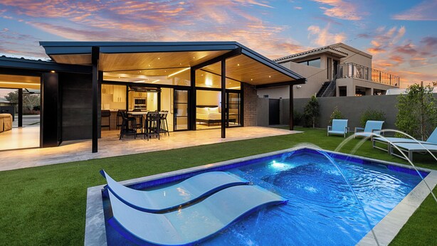 Una casa moderna con un comedor al aire libre cubierto, piscina y césped cuidado.