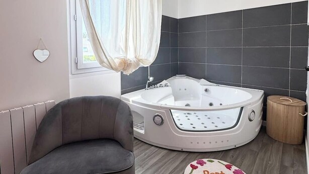 A modern bathroom with a bathtub, a chair, and a decorative rug. - Studio rose & spa – Pause bien-être (Quéven)