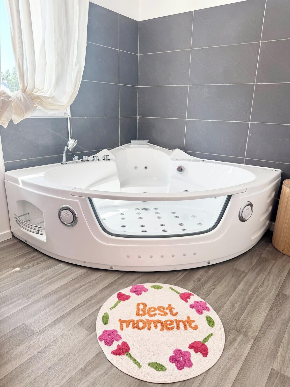 Une salle de bain moderne avec une baignoire sur pieds, des murs recouverts de carreaux foncés et un plancher en bois.