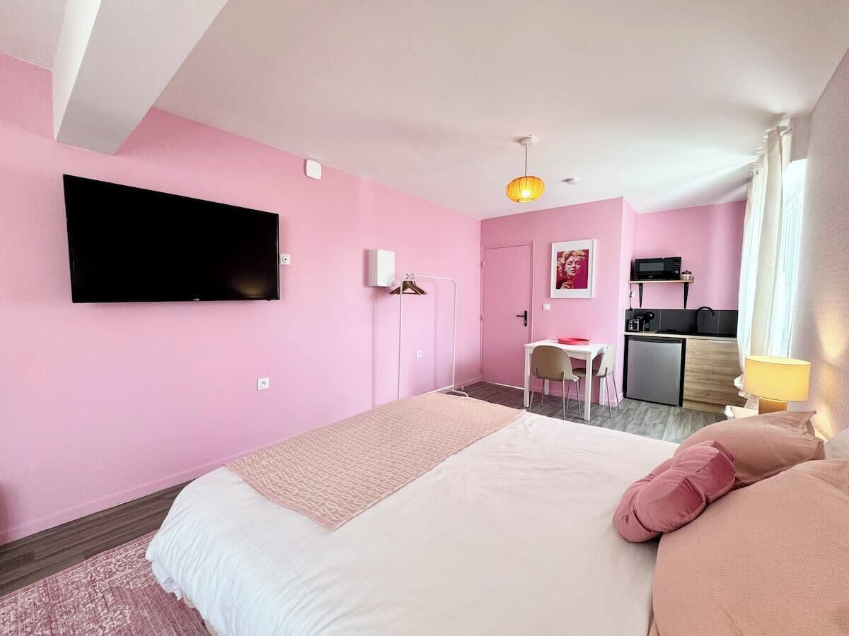 A pink-themed hotel room with a bed, a desk, and a kitchenette.