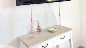 A television mounted on a white wall with a small table below it. - L’instant rose - Cocon fleuri avec jacuzzi (Quéven)