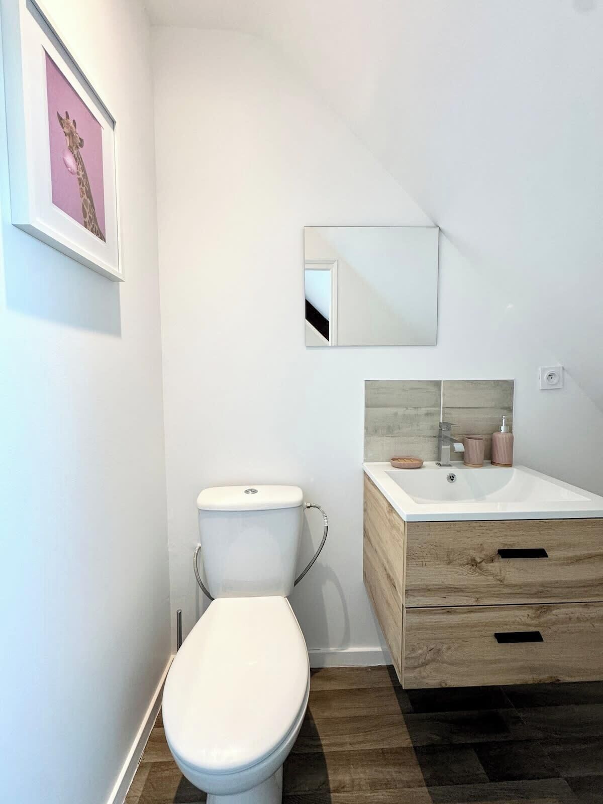 Un baño moderno con inodoro blanco, tocador de madera con lavamanos y espejo sobre el tocador.