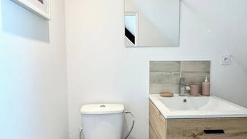 Un baño moderno con inodoro blanco, tocador de madera con lavamanos y espejo sobre el tocador.