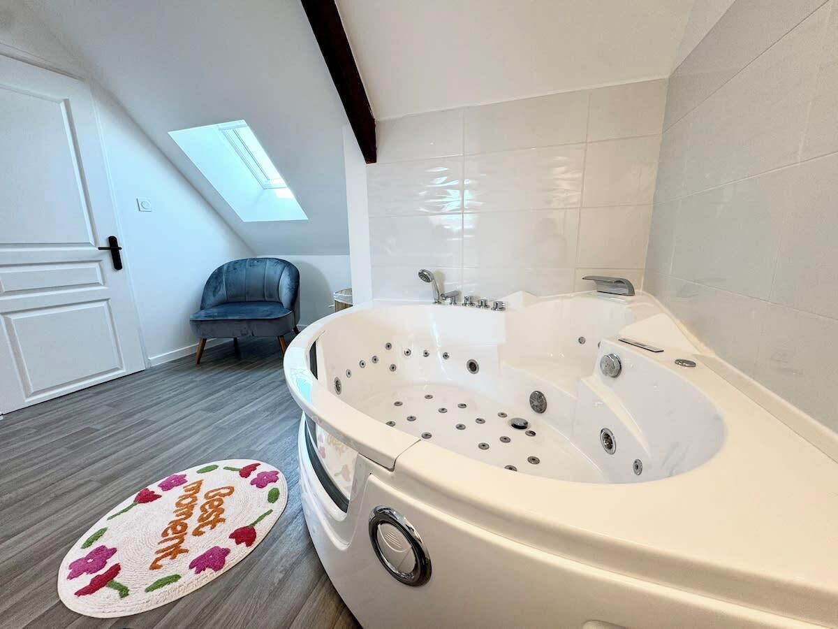 A modern bathroom with a large bathtub, a skylight, and a grey sofa.