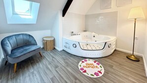 A modern bathroom with a freestanding bathtub, a round rug with 'Best moment' text, a floor lamp, and a blue sofa. - L’instant rose - Cocon fleuri avec jacuzzi (Quéven)