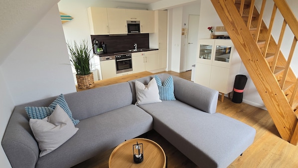 A modern living room with a grey sectional sofa, a wooden coffee table, and a kitchen in the background.
