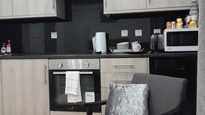 Cocina compacta con horno empotrado, microondas y un pequeño comedor con una silla y mesa.