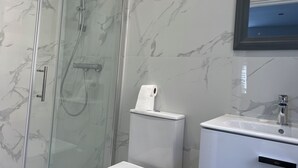 Un baño con ducha de vidrio, inodoro y lavamanos con espejo.