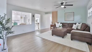 Un salon spacieux avec un canapé en cuir marron, un tapis blanc et un ventilateur de plafond.