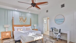 Une chambre à coucher comprenant un lit, des tables de chevet, un bureau, une chaise, un ventilateur de plafond et une œuvre d’art accrochée au mur.