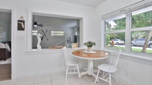 Une pièce moderne avec un intérieur blanc, une table ronde en bois, deux chaises blanches et une fenêtre donnant sur la rue.