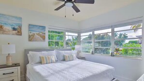 Ein Schlafzimmer mit einem großen Bett, zwei Nachttischen, einem Deckenventilator und großen Fenstern mit Blick auf Grünflächen.