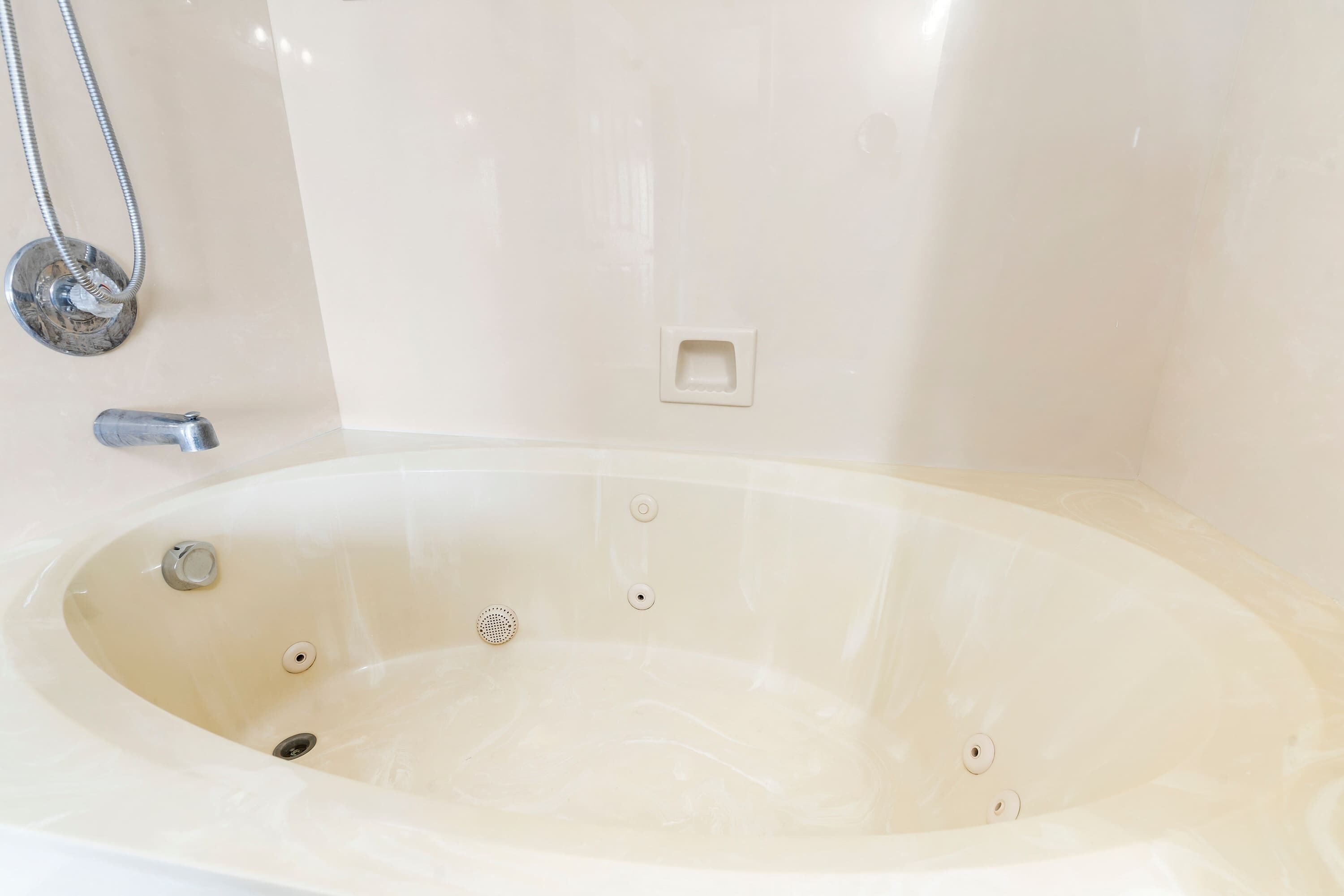A large, empty bathtub with a showerhead and faucet, a control panel, and a drain.