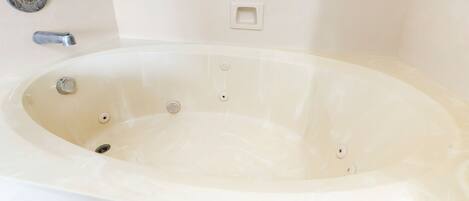 A large, empty bathtub with a showerhead and faucet, a control panel, and a drain.