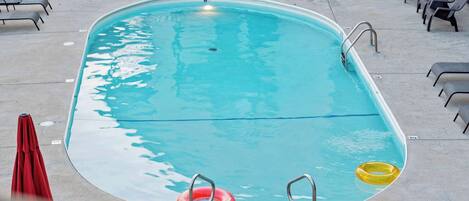 A rectangular swimming pool with a clear blue water surface, surrounded by lounge chairs and a red umbrella.