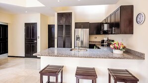 A modern kitchen with dark cabinetry, a granite countertop, and a clock on the wall.