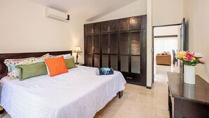 A hotel room with a bed, a ceiling fan, a wardrobe, a desk, and a vase with flowers.