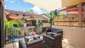 A covered outdoor patio with wicker furniture, a pool, and a bamboo fence.