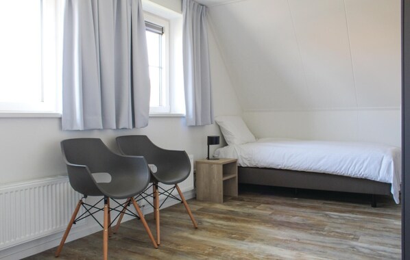 A bedroom with a bed, two chairs, a nightstand, a lamp, and a window with curtains.
