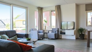 A modern living room with a sofa, two armchairs, a coffee table, a TV, and a potted plant. - Lovely Home In Idskenhuizen - With Sauna (Idskenhuizen)
