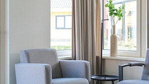 A modern hotel room with a grey armchair, a small round table, and a potted plant on a windowsill. - Lovely Home In Idskenhuizen - With Sauna (Idskenhuizen)