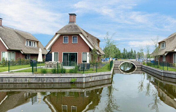 A canal-side residential area with brick houses, a bridge, and a calm water body reflecting the surroundings.