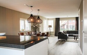 A modern kitchen with a large island, dining area with chairs and a table, and a living room with a sofa and coffee table.