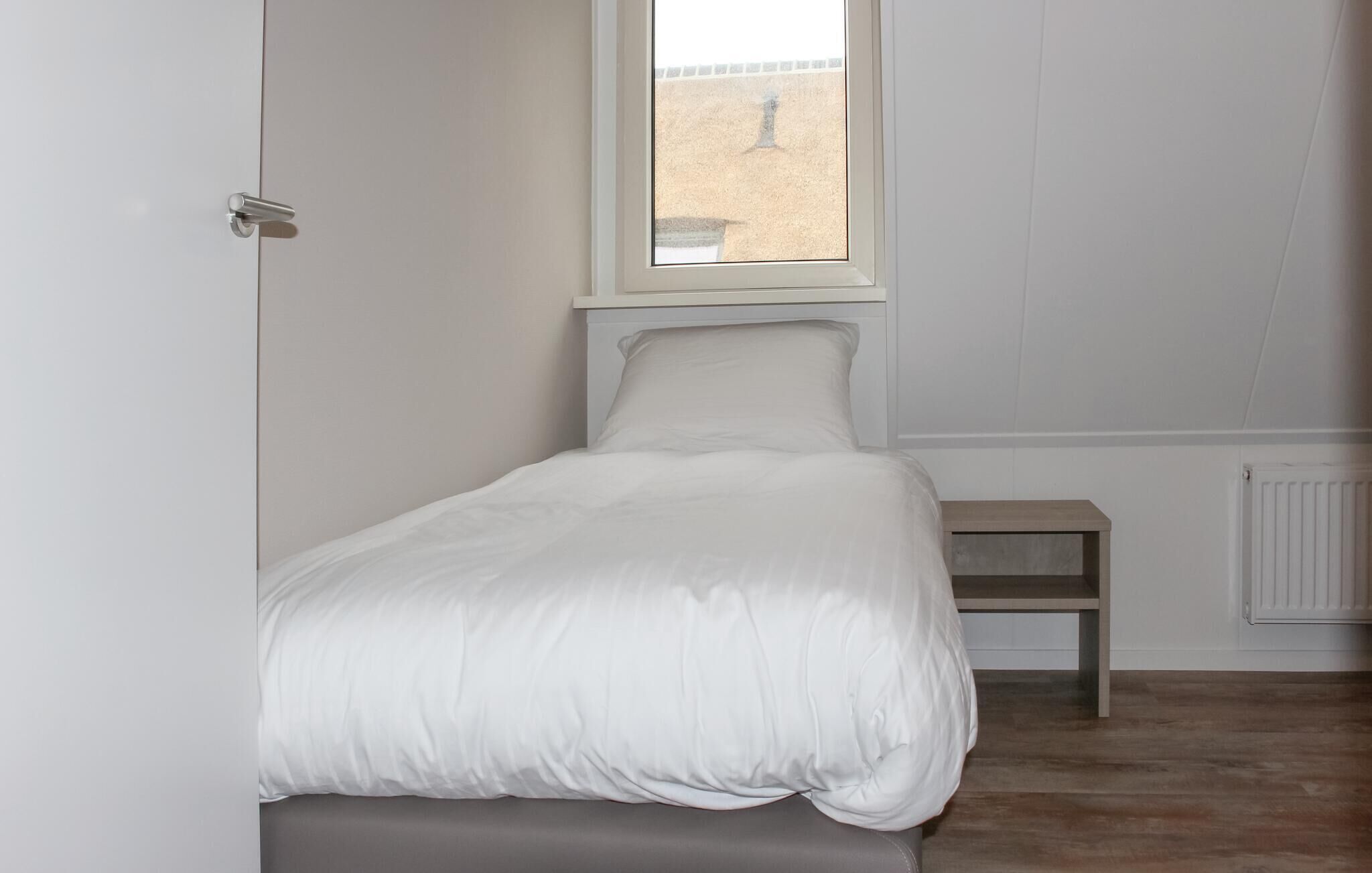 A small, neatly made bed in a room with white walls and a window.