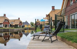 A canal-side deck with two lounge chairs, a boat, and traditional houses with thatched roofs.