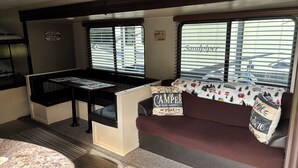 Ein gemütliches Wohnmobil-Interieur mit Küchenzeile, Essbereich und Sitzecke, inklusive Kissen mit Camping-Motiv.