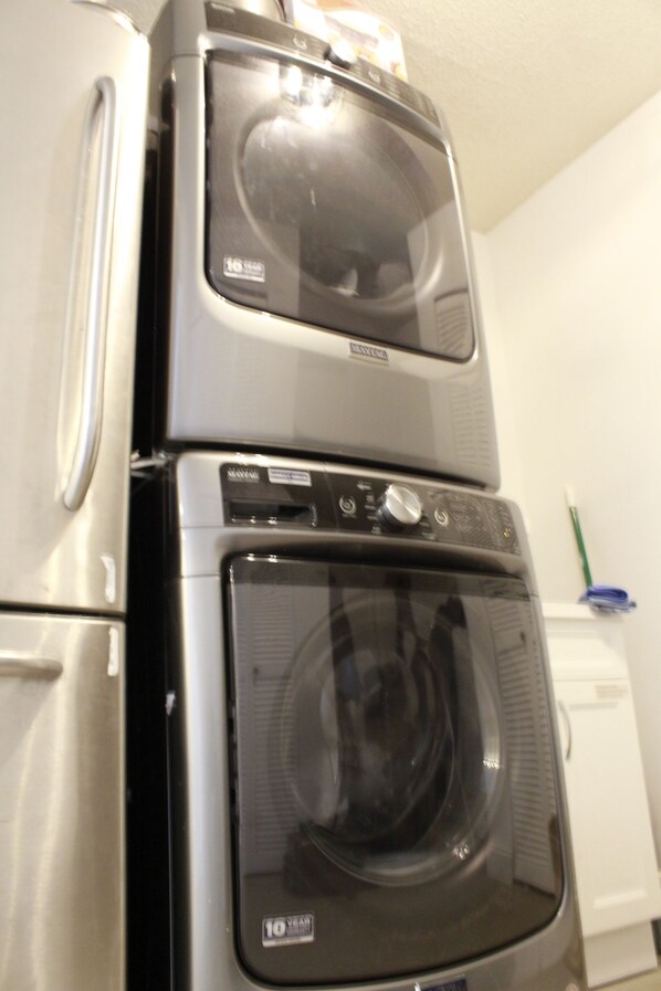 A stacked washer and dryer in a room with a white wall and a small shelf with items.