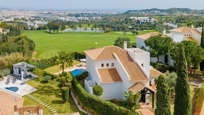 A residential area with a large house featuring a tiled roof, a swimming pool, and a well-maintained lawn.