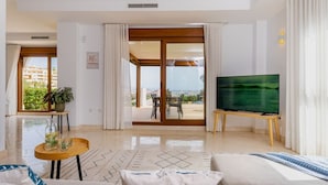 A modern living room with a large TV, a sofa, a coffee table, and a view of the outdoors through a sliding glass door.
